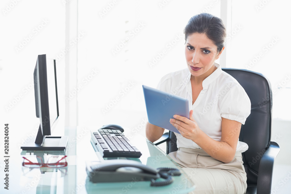 Stern businesswoman using her digital tablet at desk Stern businesswoman using her digital tablet at desk