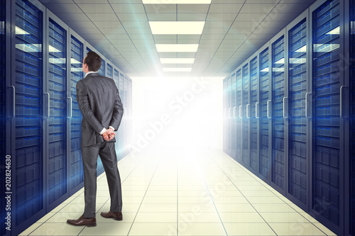Businessman in grey suit looking against digitally generated server room with towers
