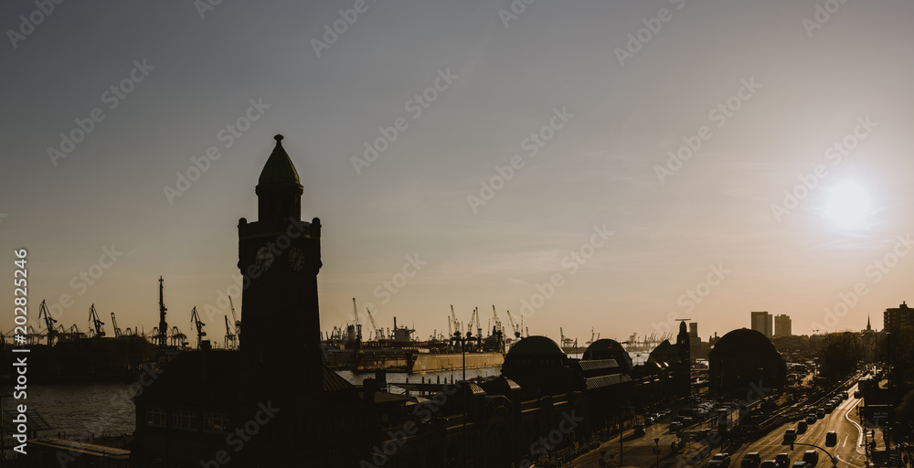 Silhouette of famous Hamburger Landungsbruecken with commercial harbor and Elbe river with evening sun, St. Pauli district, Hamburg, Germany