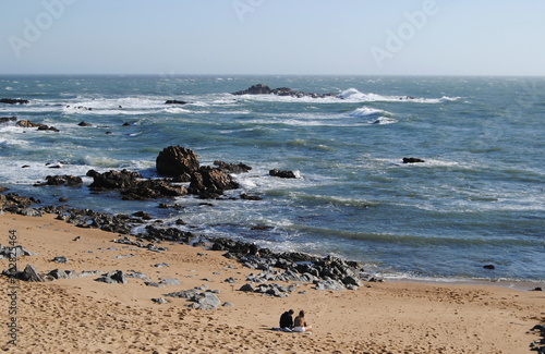 Tertulia á beira mar, casal jovem sentado na praia na areia do mar a namorar e a conversar, local romântico