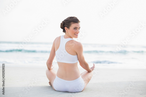 Content slim brown haired model in white sportswear meditating in lotus position