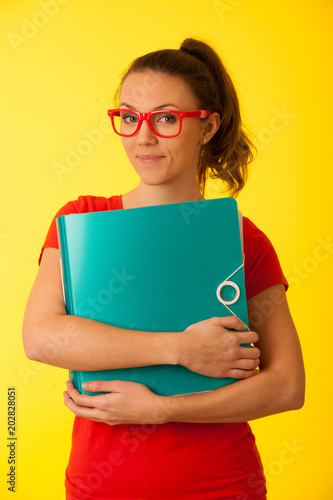 Young geek student woman in red t shirt hold a folder over yellow background