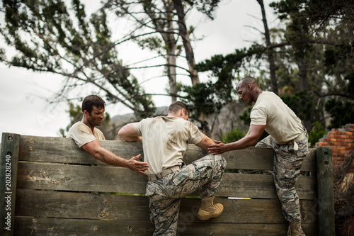 Soldiers helping man to climb wooden wall