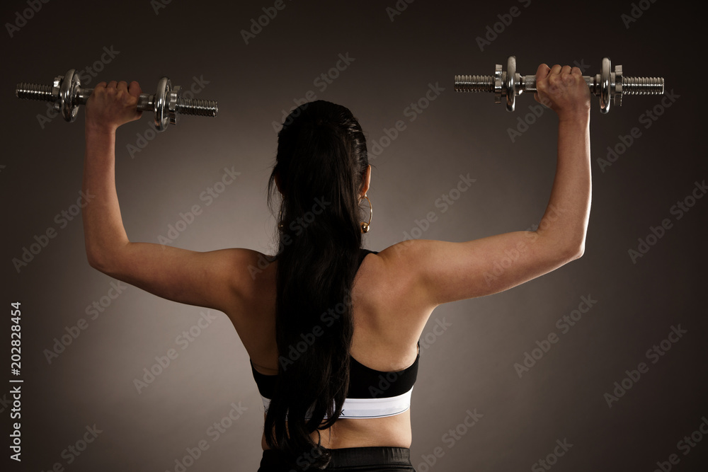 Woman work out arms with dumbbells over gray background