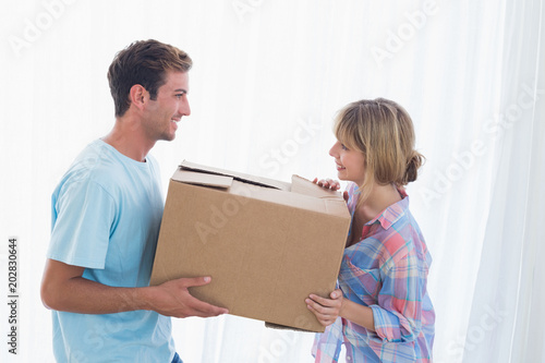 Smiling couple carrying cardboard box in new house
