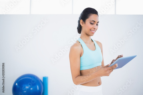 Pretty sporty woman standing in fitness hall using her tablet