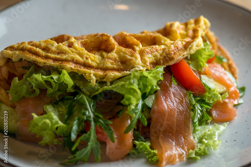 French omelette on a white dish. Omelette in French with salad Iceberg, salmon and greens. Dietary omelette with herbs for breakfast