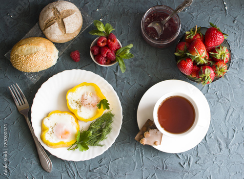 Breakfast with scrambled eggs, raspberries, strawberries and a jar of jam, cap of tea and chocolate