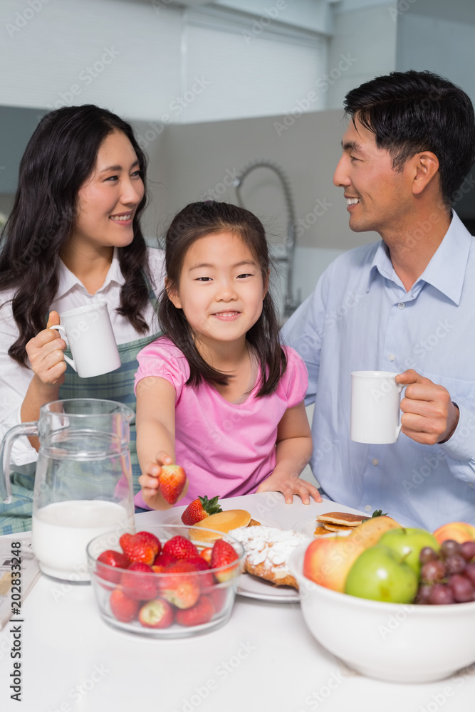 Portrait of a young girl enjoying breakfast with parents Portrait of a young girl enjoying breakfast with parents