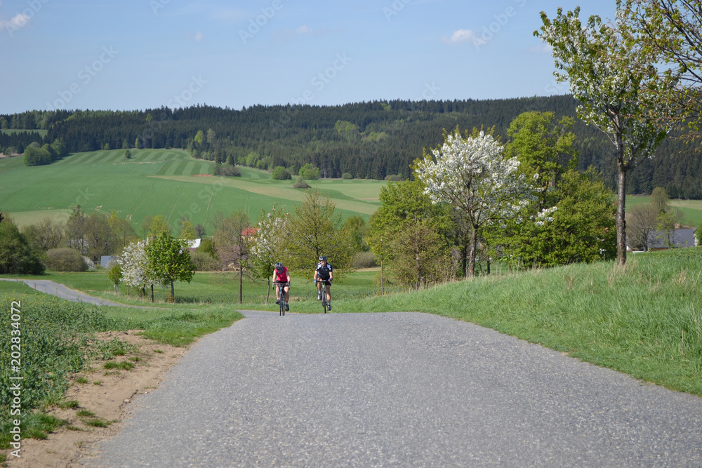 Fototapeta premium Spring bike riding on the beautiful hills, Young couple on bikes riding on the beautiful green hills during beautiful spring day