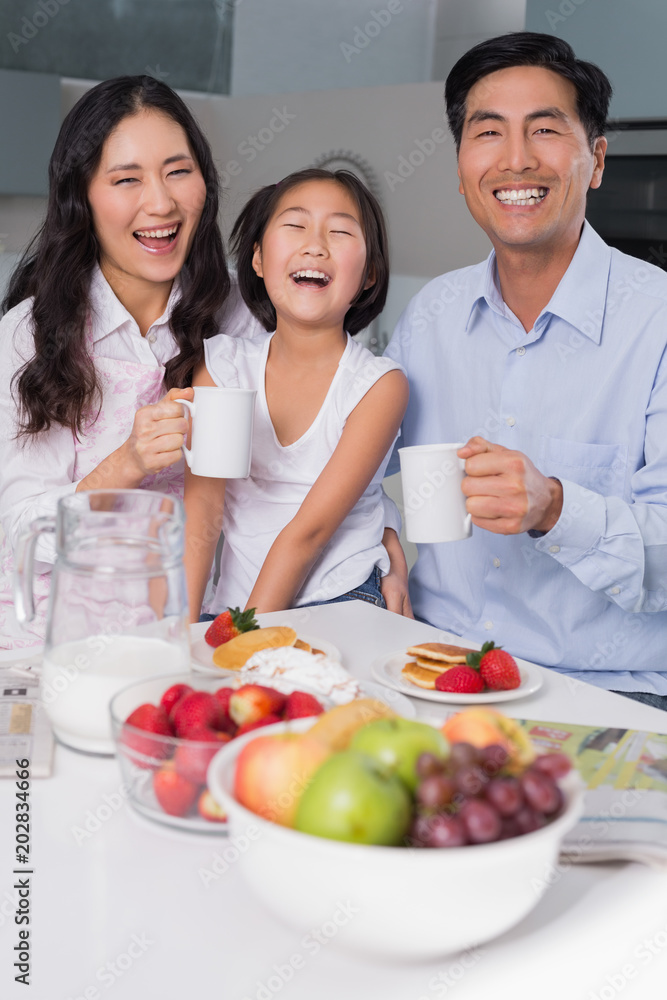 Cheerful young girl enjoying breakfast with parents Cheerful young girl enjoying breakfast with parents