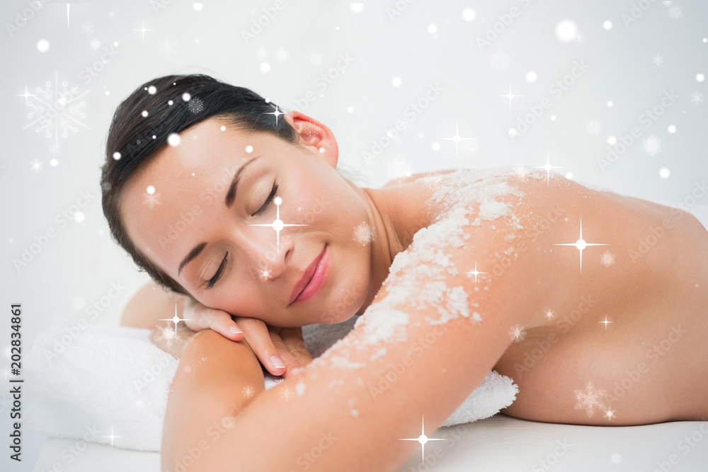 Peaceful brunette lying with salt scrub on shoulders against snow falling Peaceful brunette lying with salt scrub on shoulders against snow falling