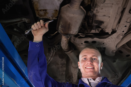 Mechanic looking at camera below a car