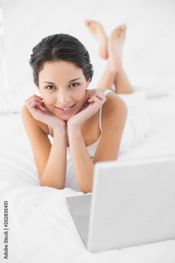 Content casual brunette in white pajamas lying on her bed and looking at camera Content casual brunette in white pajamas lying on her bed and looking at camera