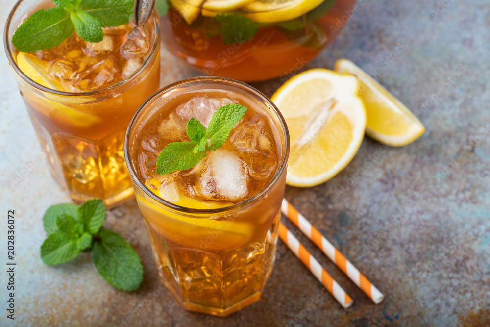 Traditional iced tea with lemon, mint and ice in tall glasses. Two glasses with cool summer drink on old rusty background Traditional iced tea with lemon, mint and ice in tall glasses. Two glasses with cool summer drink on old rusty background