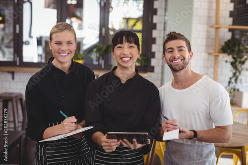 Portrait of smiling young wait staff holding digital tablet with notepad and clipboard