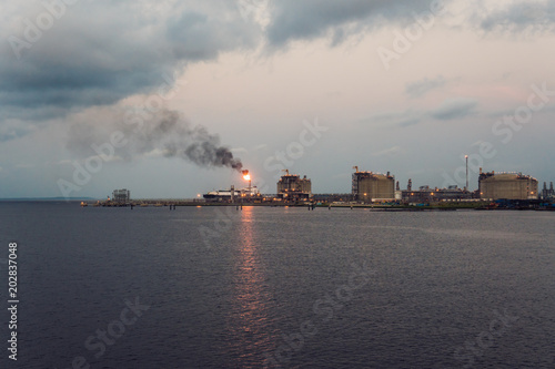 gas and oil refinery industry factory at marine port. Fire flare is burning on the up of building.