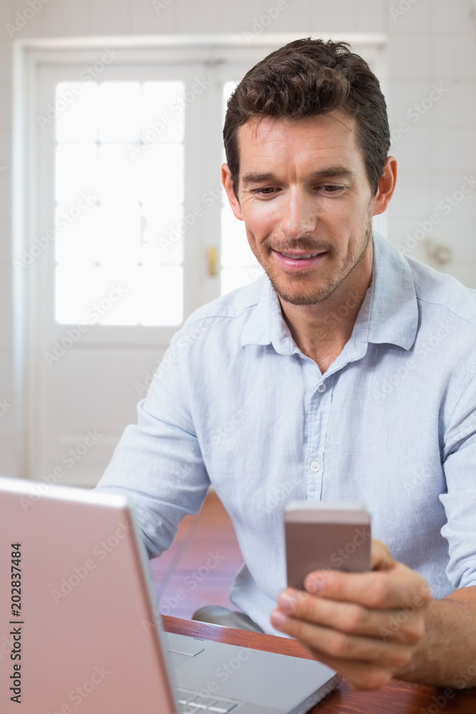 Smiling young man using laptop and mobile phone Smiling young man using laptop and mobile phone