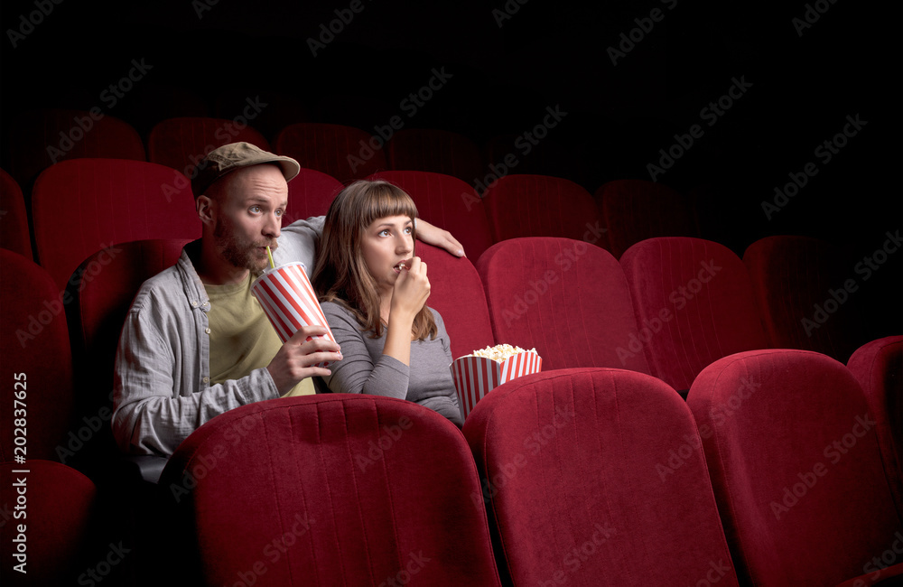 Young cute couple sitting alone at red movie theatre and having fun Young cute couple sitting alone at red movie theatre and having fun