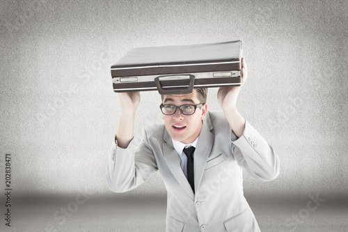 Geeky businessman holding his briefcase over head against grey room