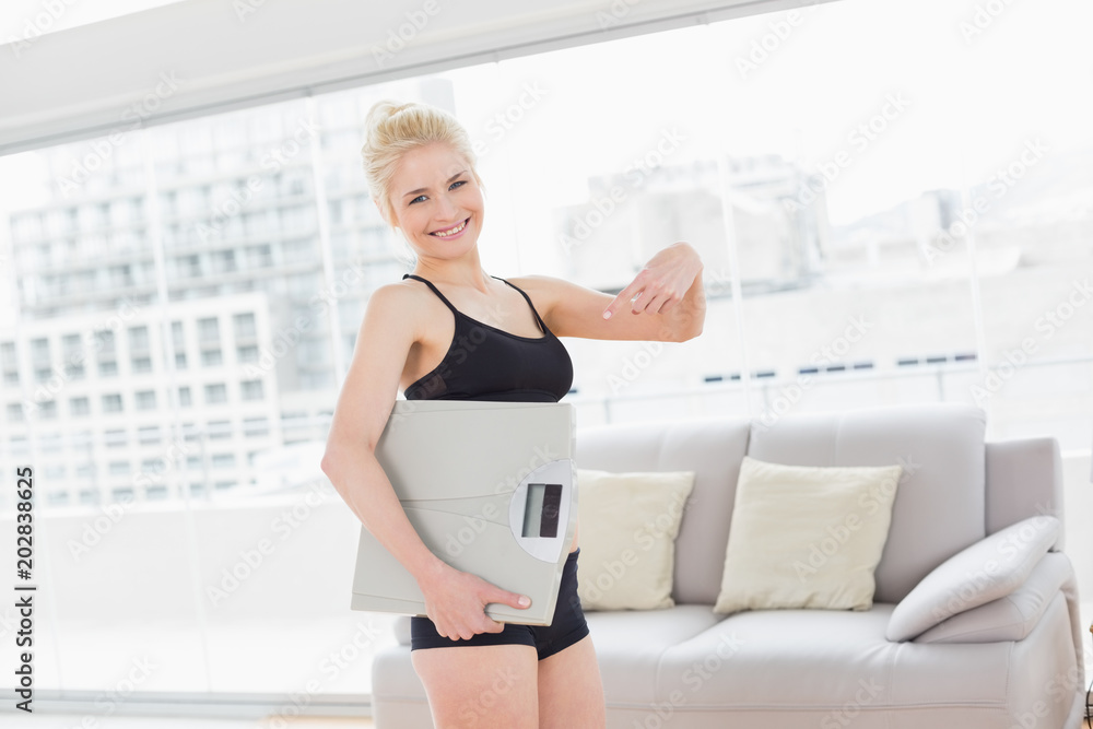 Woman in sportswear carrying scale in fitness studio Woman in sportswear carrying scale in fitness studio