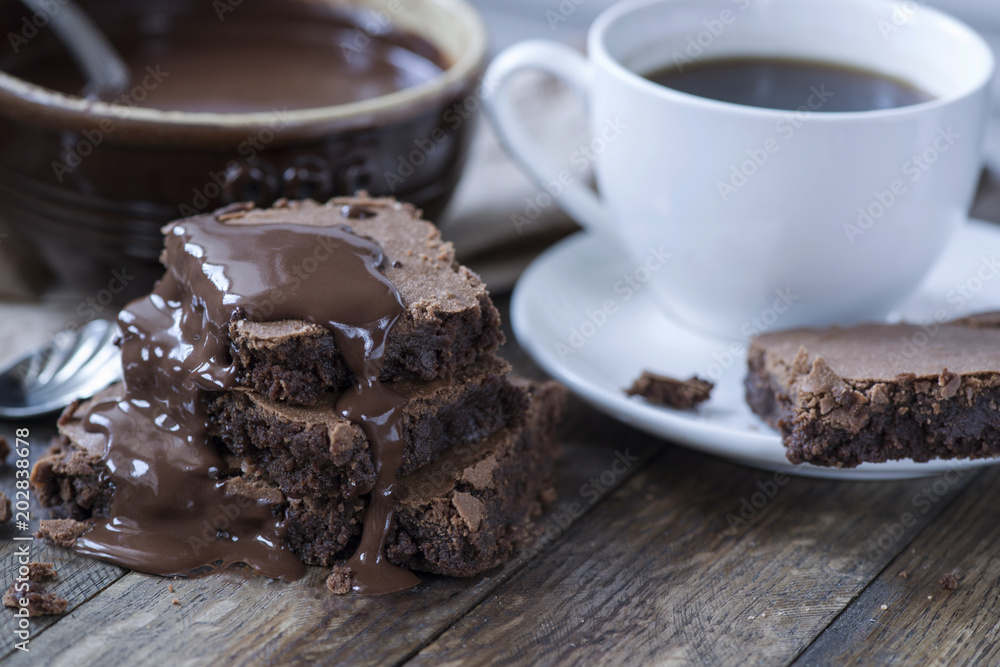 Homemade chocolate brownies with coffee on wooden background, chocolate souce on ceramic bowl Homemade chocolate brownies with coffee on wooden background, chocolate souce on ceramic bowl