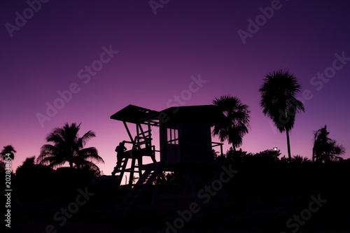 Silhouette of baywatch tower and palm trees at sunset in Playa del Carmen, Mexico. Lifeguard wooden structure at twilight by Caribbean Sea. Summer travel destination, tourism concept