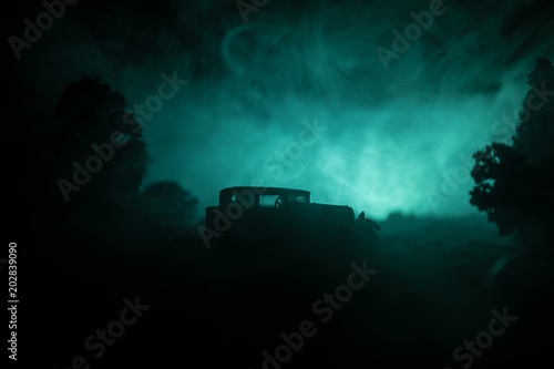 Silhouette of old vintage car in dark foggy toned background with glowing lights in low light, or silhouette of old car in dark forest.