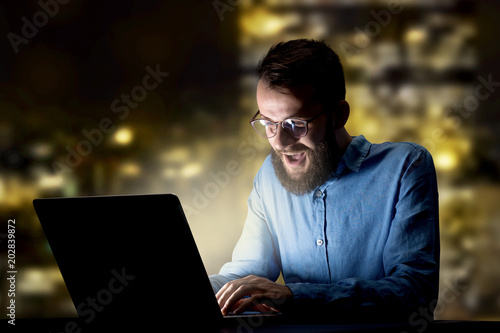 Young handsome businessman working late at night in the office with city lights in the background © ra2 studio