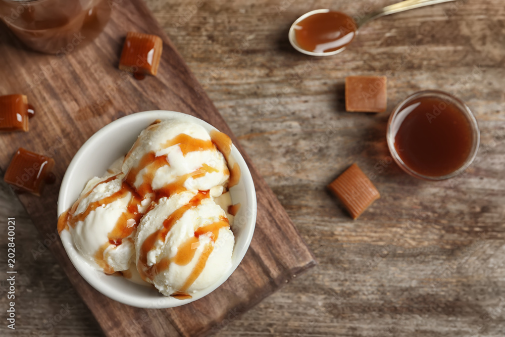 Tasty ice cream with caramel sauce in bowl on wooden board