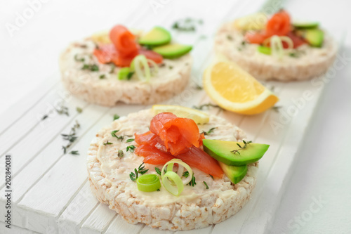 Crispbreads with fresh sliced salmon fillet and avocado on wooden board, closeup