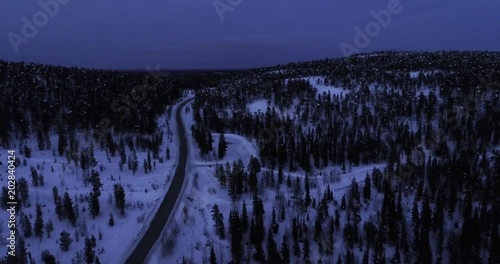 Road in the wild, C4k aerial view over a route, between tunturi fjelds and snowy taiga wilderness, on a sunny winter evening dawn, in Pyha-luosto national park, Lapland, Finland photo