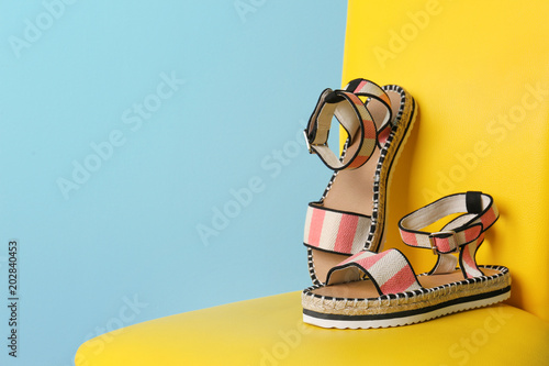 Pair of female shoes on chair against color background