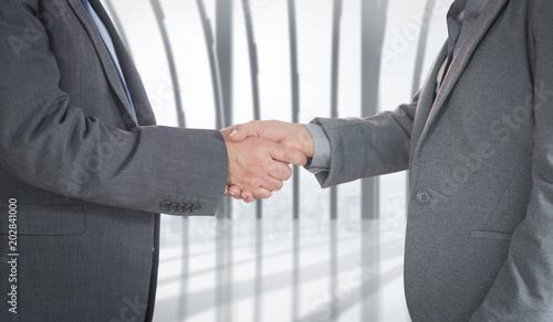 Close up on two businesspeople shaking hands against white room with large window overlooking city