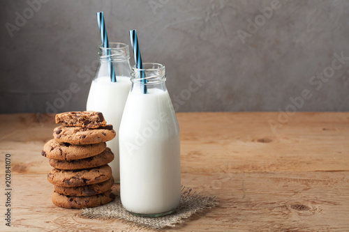 Two bottles of milk and chocolate chip cookies on dark background with copy space photo