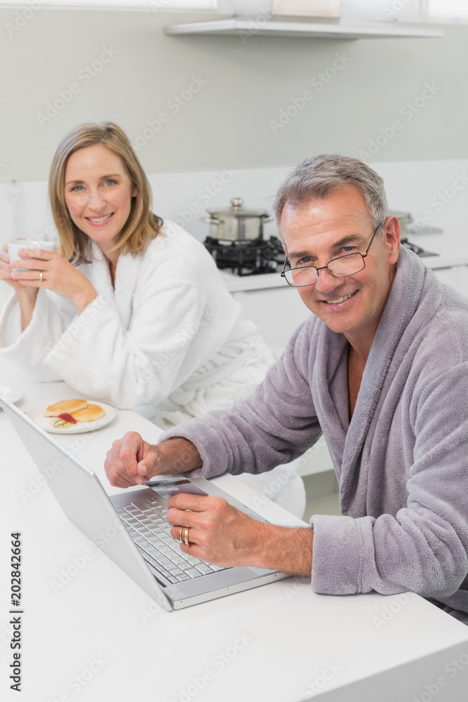 Happy couple in bathrobe doing online shopping at home Happy couple in bathrobe doing online shopping at home