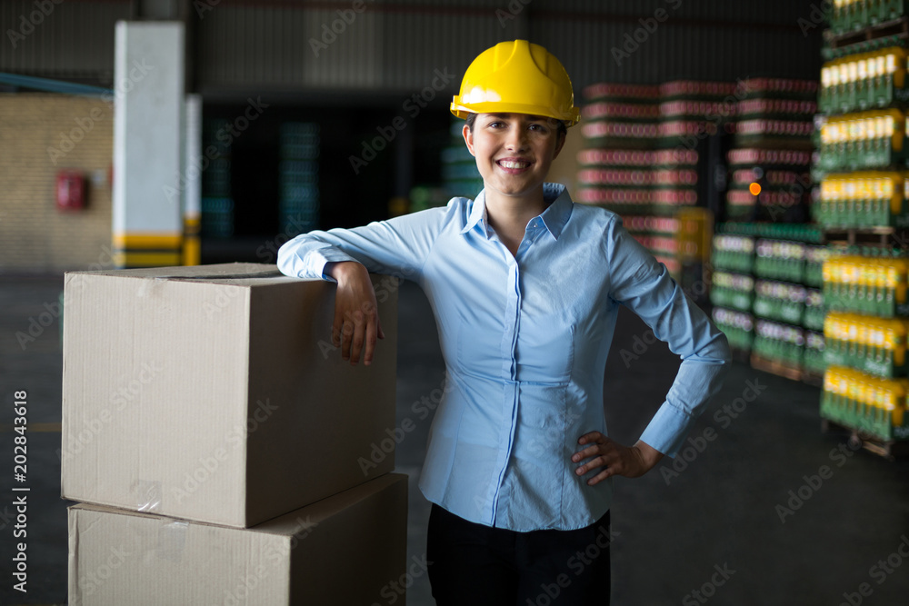 Smiling female factory worker standing with hand on hip in factory Smiling female factory worker standing with hand on hip in factory