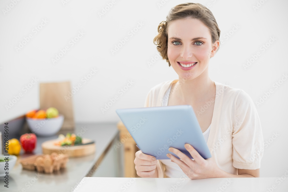 Happy beautiful woman holding her tablet sitting in her kitchen at home Happy beautiful woman holding her tablet sitting in her kitchen at home