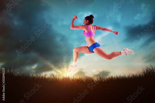 Fit brunette running and jumping against blue sky over grass