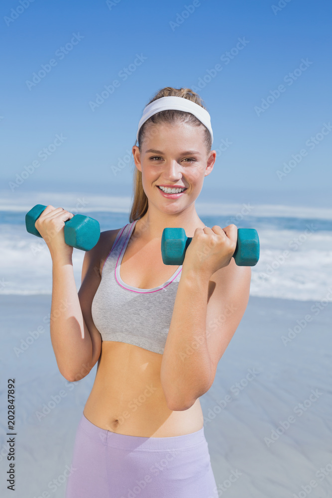 Sporty happy blonde lifting dumbbells on the beach Sporty happy blonde lifting dumbbells on the beach