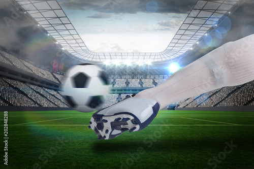 Composite image of close up of football player kicking ball against large football stadium with lights