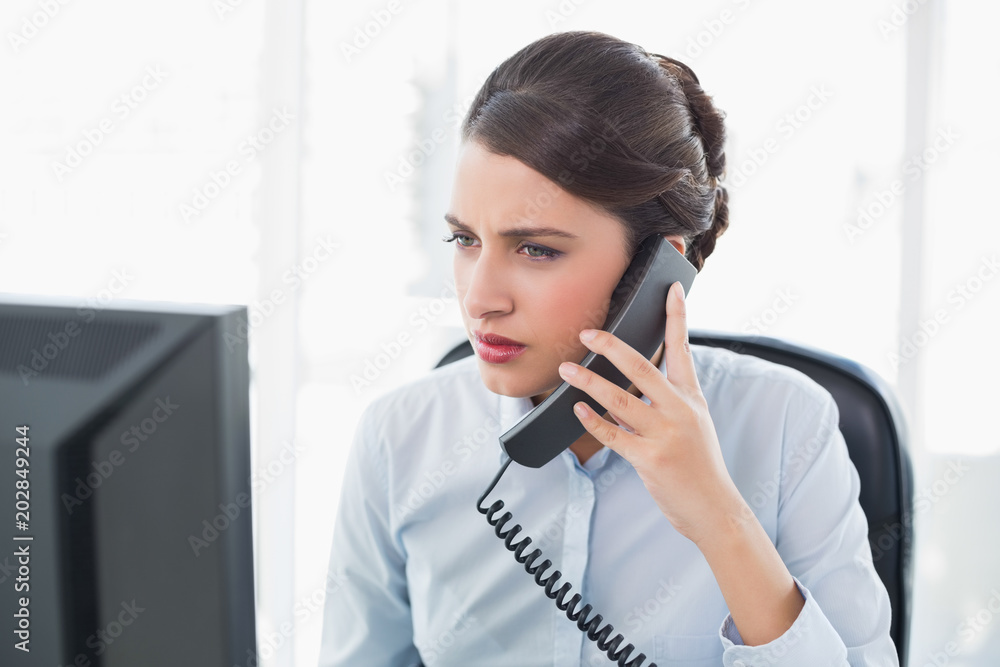 Stern classy brown haired businesswoman answering the telephone Stern classy brown haired businesswoman answering the telephone