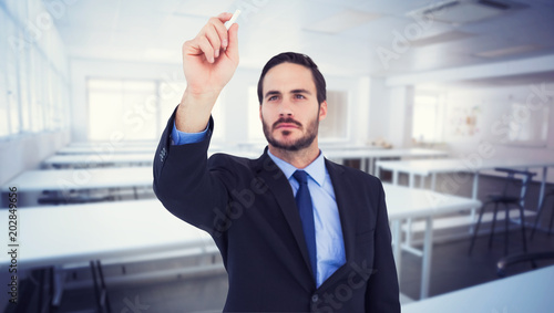 Businessman holding a chalk and writing something against empty class room 