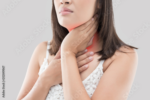 Asian woman with sore throat or neck pain or thyroid gland against gray background. People body problem concept