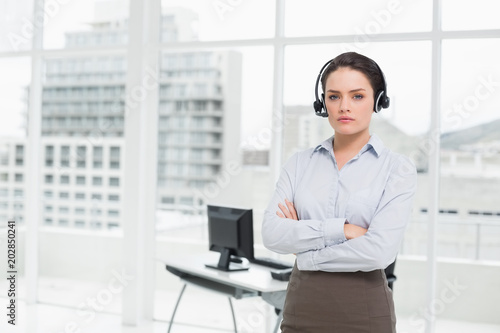 Elegant businesswoman wearing headset with arms crossed in office