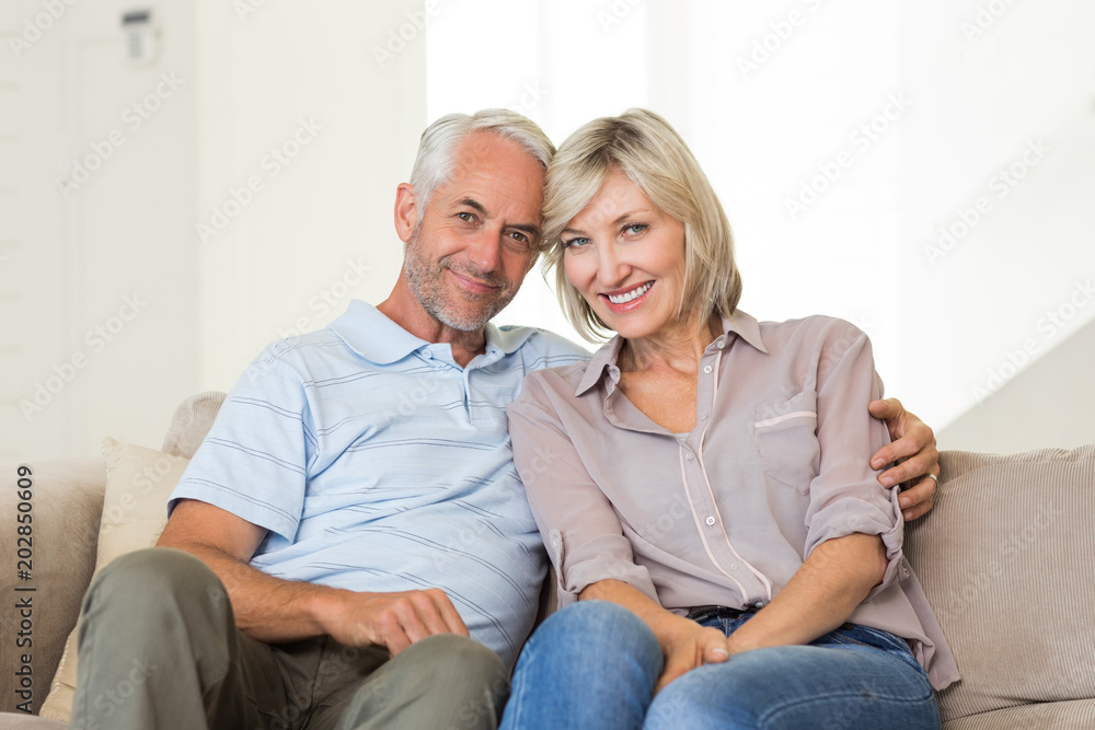 Smiling mature couple sitting on sofa with arm around Smiling mature couple sitting on sofa with arm around