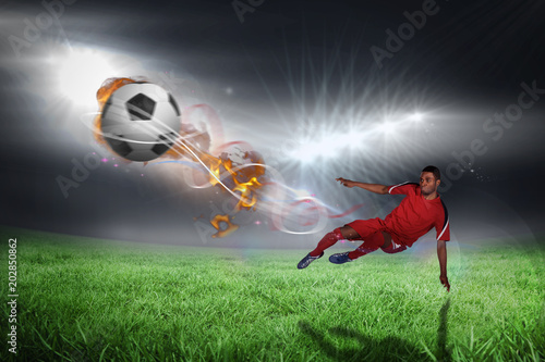 Football player in red kicking against football pitch under bright lights © vectorfusionart