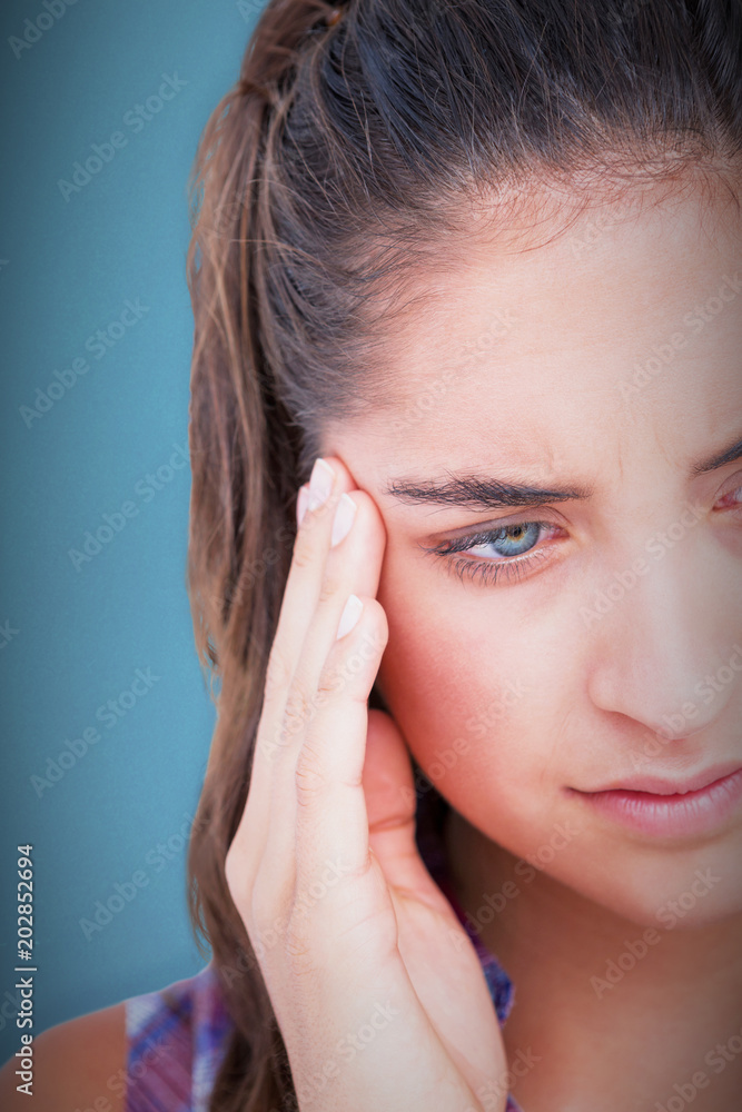 Close-up of beautiful woman suffering from headache against blue background Close-up of beautiful woman suffering from headache against blue background