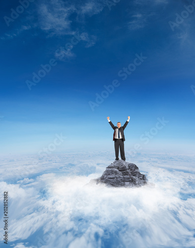Mature businessman cheering with arms up against mountain peak through the clouds