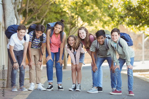 Portrait of happy students standing with schoolbag on road